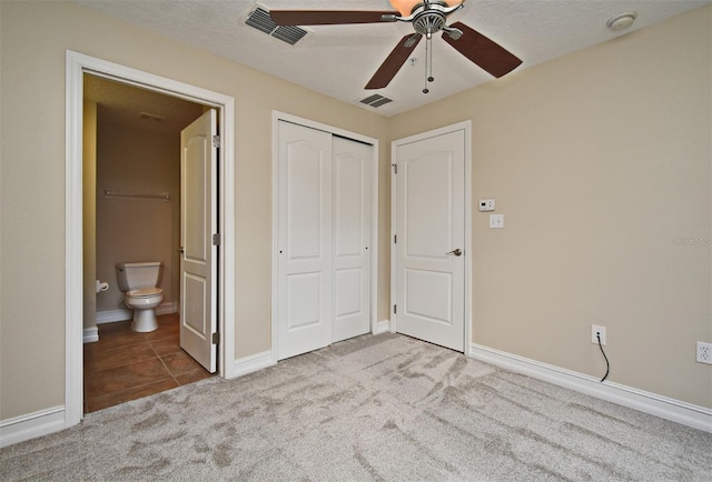 unfurnished bedroom with ceiling fan, ensuite bathroom, a textured ceiling, light colored carpet, and a closet