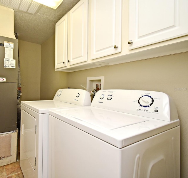 laundry room with light tile patterned floors, cabinets, independent washer and dryer, heating unit, and a textured ceiling