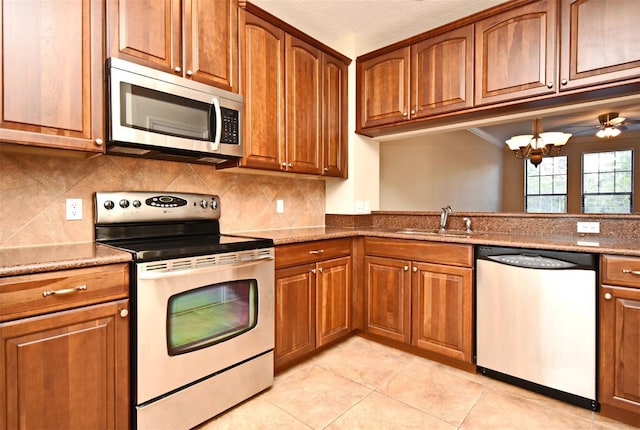 kitchen with sink, appliances with stainless steel finishes, light stone counters, decorative backsplash, and a chandelier