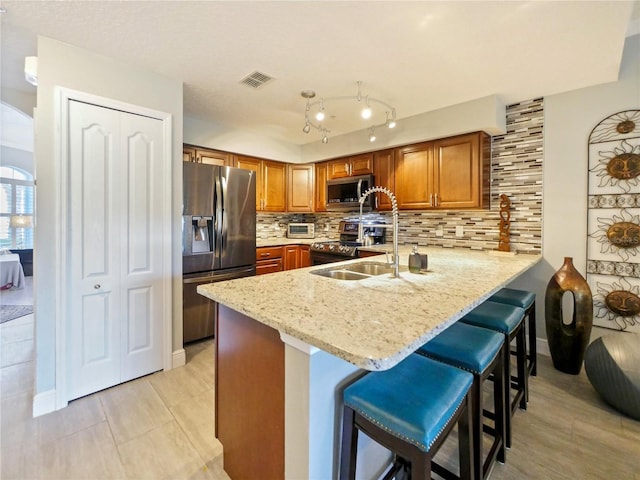 kitchen featuring stainless steel appliances, a peninsula, a sink, visible vents, and brown cabinetry