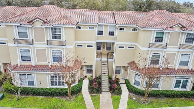 townhome / multi-family property with stairs, a tile roof, a residential view, and stucco siding