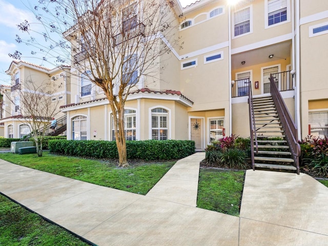 multi unit property featuring a tiled roof, a front yard, stairway, and stucco siding