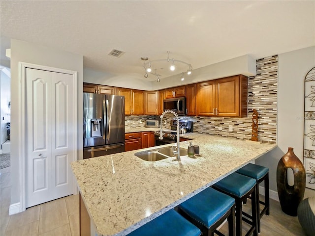 kitchen with brown cabinets, stainless steel appliances, decorative backsplash, a sink, and a peninsula