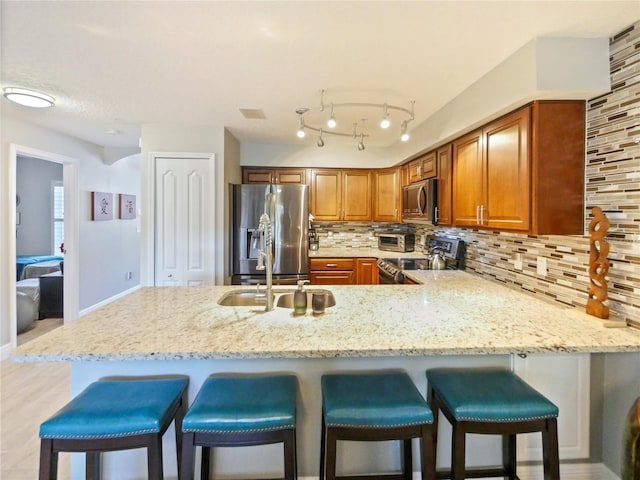 kitchen featuring tasteful backsplash, brown cabinetry, appliances with stainless steel finishes, light stone counters, and a peninsula