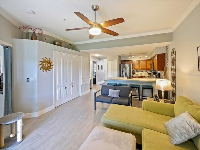 living room with ornamental molding, light wood-style floors, baseboards, and a ceiling fan