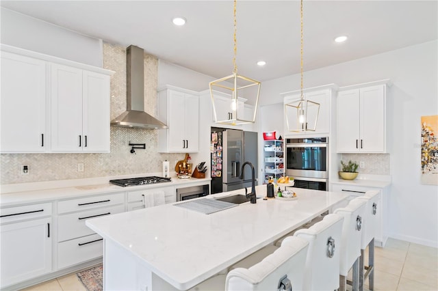 kitchen with appliances with stainless steel finishes, a kitchen island with sink, a breakfast bar area, and wall chimney range hood