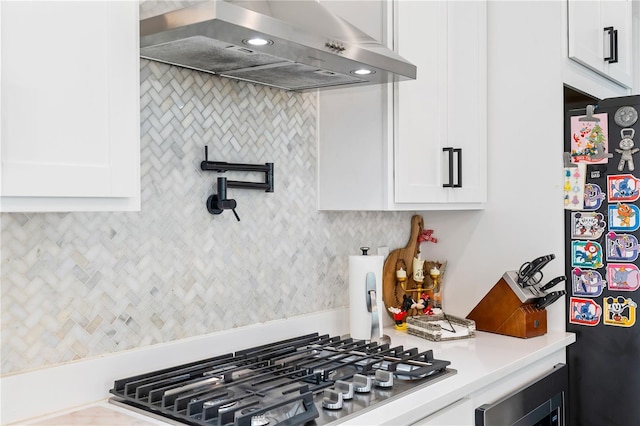 kitchen with white cabinetry, black fridge, ventilation hood, and stainless steel gas cooktop