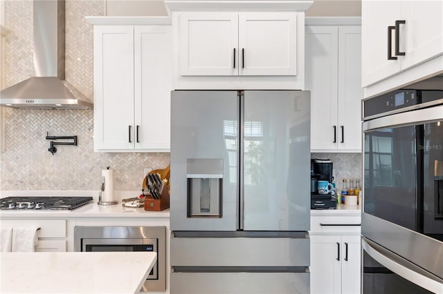 kitchen with backsplash, wall chimney exhaust hood, stainless steel appliances, and white cabinets