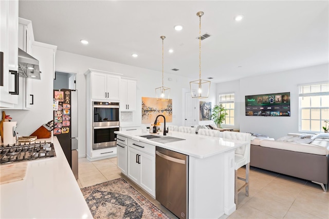 kitchen with sink, white cabinetry, decorative light fixtures, stainless steel appliances, and a kitchen island with sink