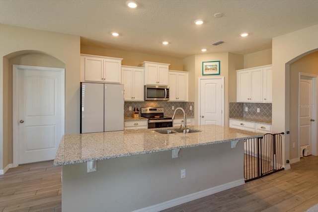 kitchen with stainless steel appliances, an island with sink, sink, and white cabinetry