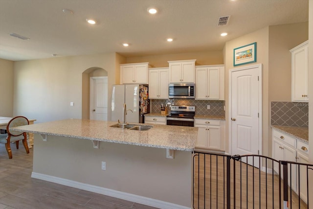 kitchen featuring light stone counters, appliances with stainless steel finishes, a breakfast bar, and an island with sink