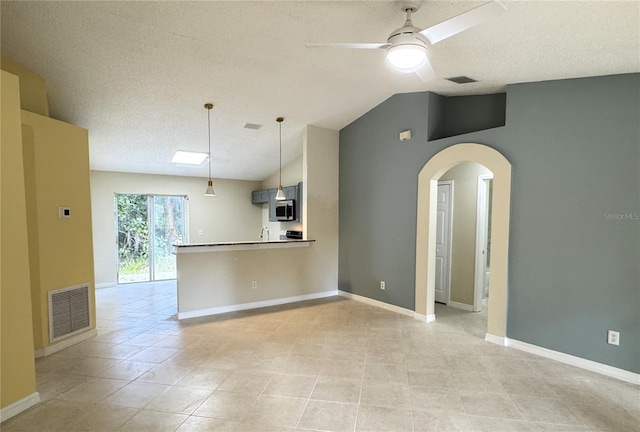 kitchen with arched walkways, visible vents, stainless steel microwave, a peninsula, and vaulted ceiling