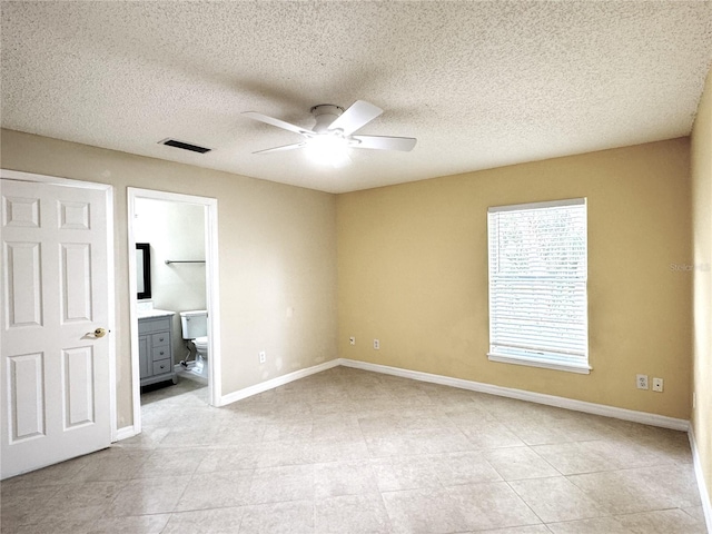 unfurnished bedroom with ensuite bath, baseboards, visible vents, and a textured ceiling