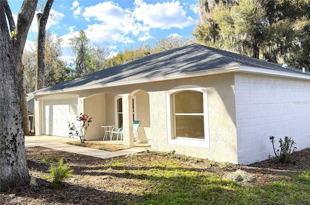 single story home featuring stucco siding, a porch, a shingled roof, a garage, and driveway