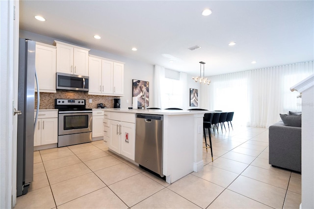 kitchen featuring white cabinetry, stainless steel appliances, decorative light fixtures, and a center island with sink