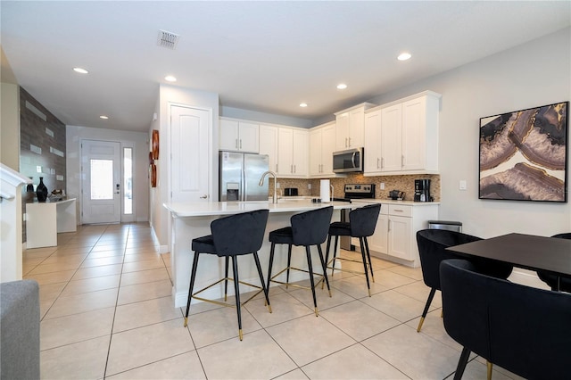 kitchen featuring a breakfast bar, white cabinetry, stainless steel appliances, a center island with sink, and decorative backsplash