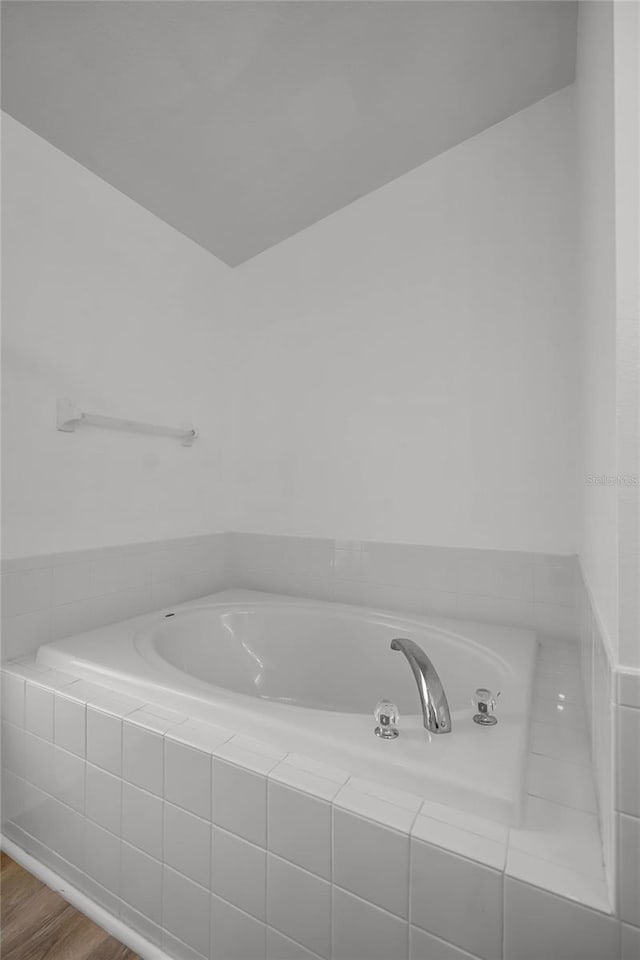 bathroom with a relaxing tiled tub and hardwood / wood-style flooring