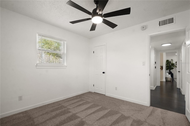 unfurnished room with a textured ceiling, ceiling fan, visible vents, baseboards, and dark colored carpet