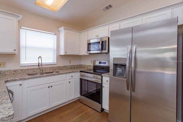 kitchen with appliances with stainless steel finishes, sink, white cabinets, and light stone counters