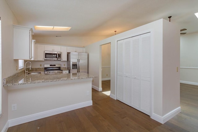 kitchen with sink, appliances with stainless steel finishes, white cabinetry, dark hardwood / wood-style floors, and light stone countertops