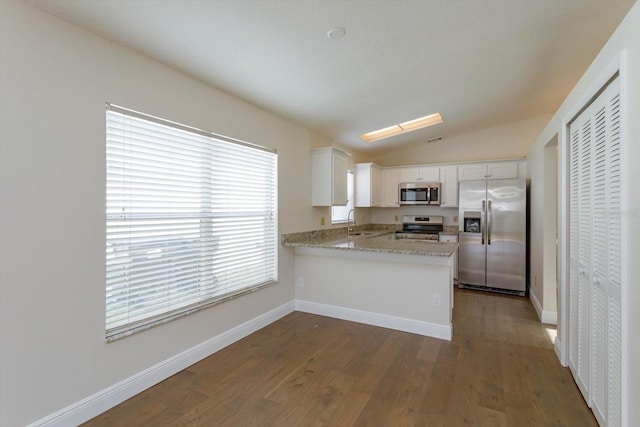 kitchen with sink, vaulted ceiling, kitchen peninsula, stainless steel appliances, and white cabinets