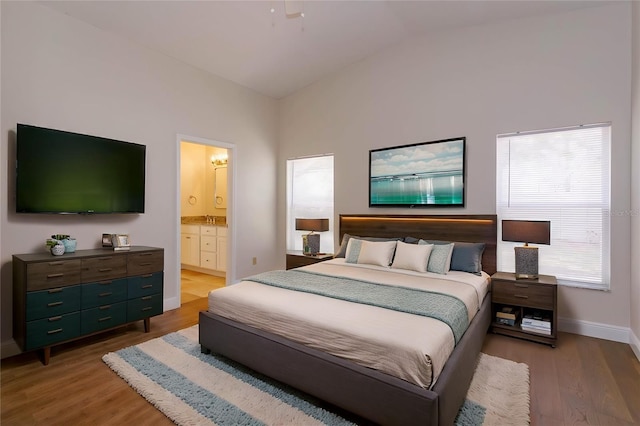 bedroom featuring ensuite bathroom, sink, vaulted ceiling, and light hardwood / wood-style flooring