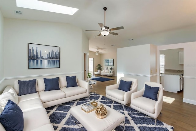 living room with wood-type flooring, lofted ceiling with skylight, and ceiling fan