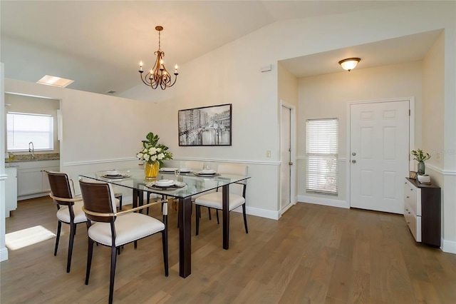 dining area with wood-type flooring, vaulted ceiling, sink, and a notable chandelier