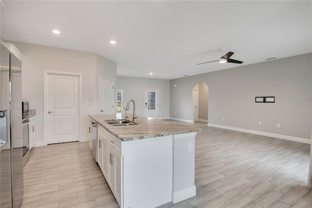 kitchen with light stone countertops, sink, a center island with sink, and white cabinets