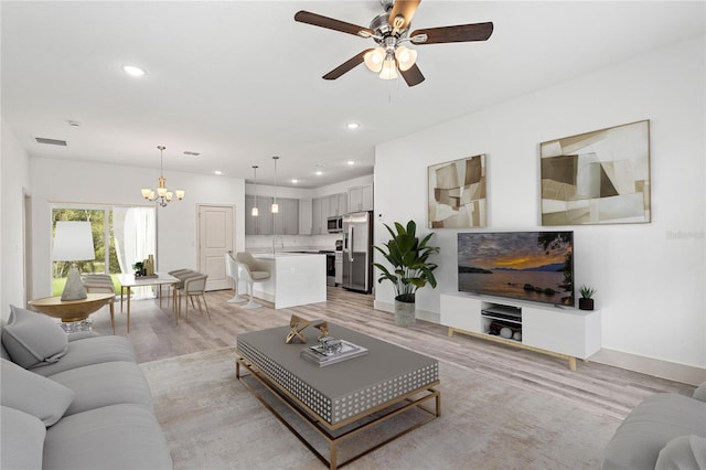 living room featuring ceiling fan with notable chandelier and light wood-type flooring