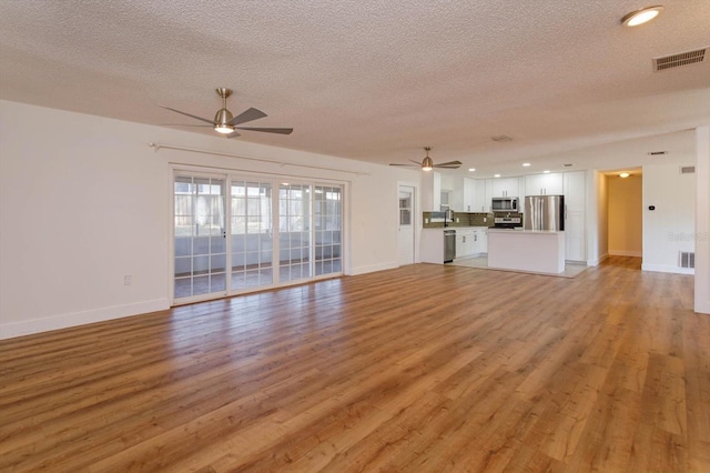 unfurnished living room featuring ceiling fan, sink, a textured ceiling, and light wood-type flooring