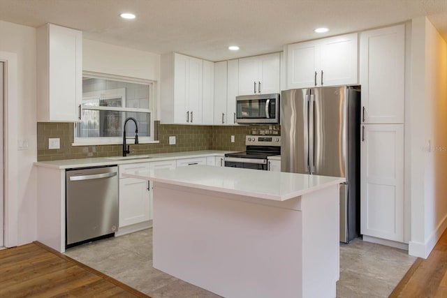 kitchen featuring sink, appliances with stainless steel finishes, a kitchen island, decorative backsplash, and white cabinets