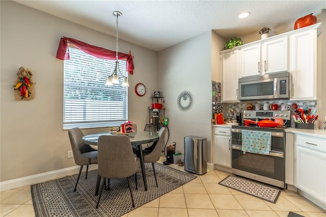 kitchen with hanging light fixtures, backsplash, stainless steel appliances, white cabinets, and light tile patterned flooring