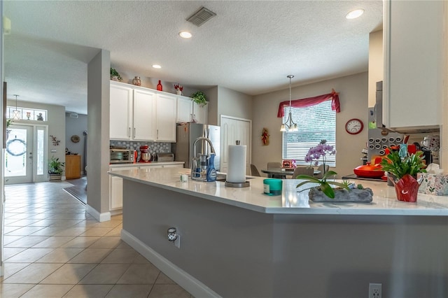 kitchen with light tile patterned floors, stainless steel refrigerator, backsplash, white cabinets, and decorative light fixtures