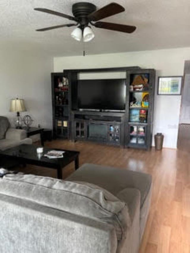 living room with ceiling fan, a textured ceiling, and wood finished floors