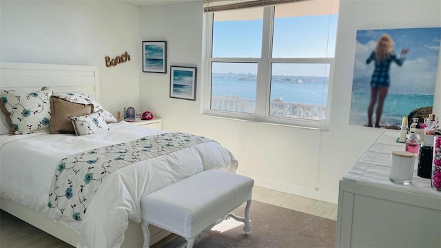 bedroom with multiple windows, a water view, and hardwood / wood-style floors