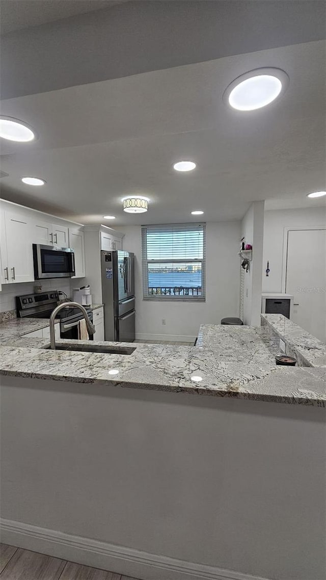 kitchen with light stone countertops, wood finished floors, white cabinets, stainless steel appliances, and a sink