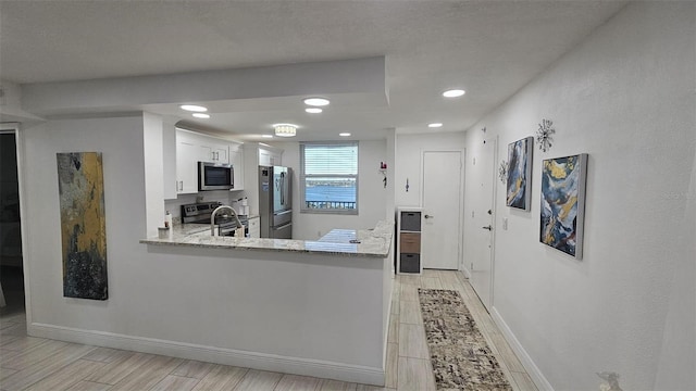 kitchen with baseboards, wood tiled floor, light stone counters, appliances with stainless steel finishes, and white cabinets