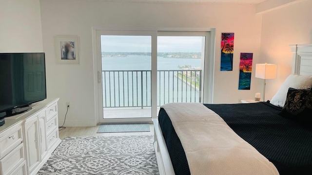 bedroom featuring access to outside, light wood-style flooring, a water view, and baseboards