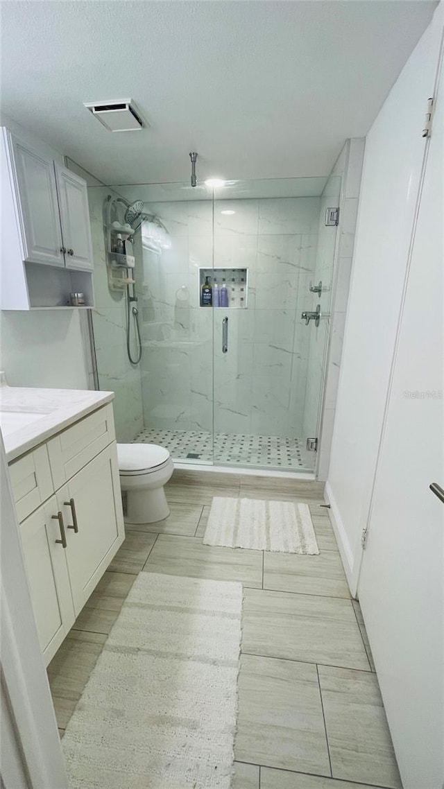 bathroom featuring a marble finish shower, visible vents, toilet, vanity, and a textured ceiling