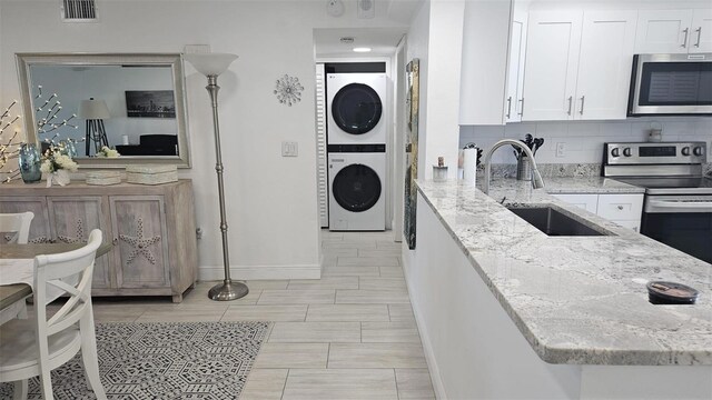 kitchen featuring visible vents, stacked washing maching and dryer, a sink, stainless steel appliances, and white cabinetry