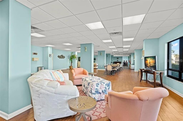 living area with visible vents, a paneled ceiling, baseboards, and wood finished floors