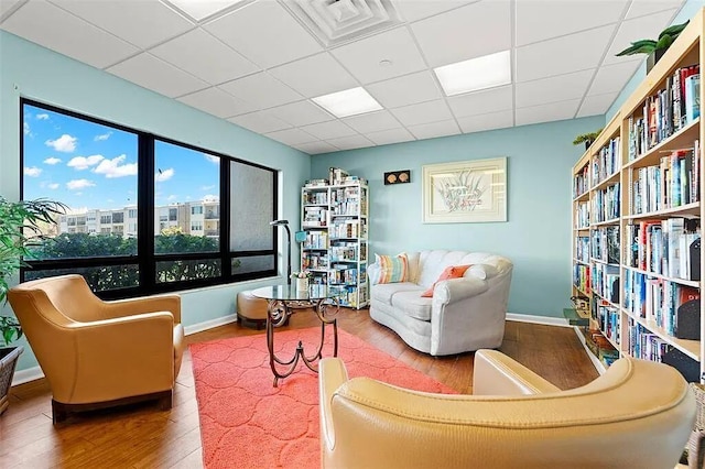 sitting room with visible vents, a drop ceiling, baseboards, and wood finished floors