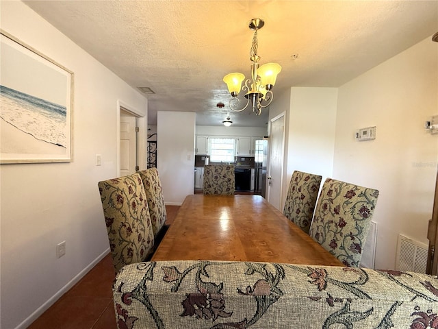 dining area with an inviting chandelier, dark tile patterned floors, and a textured ceiling