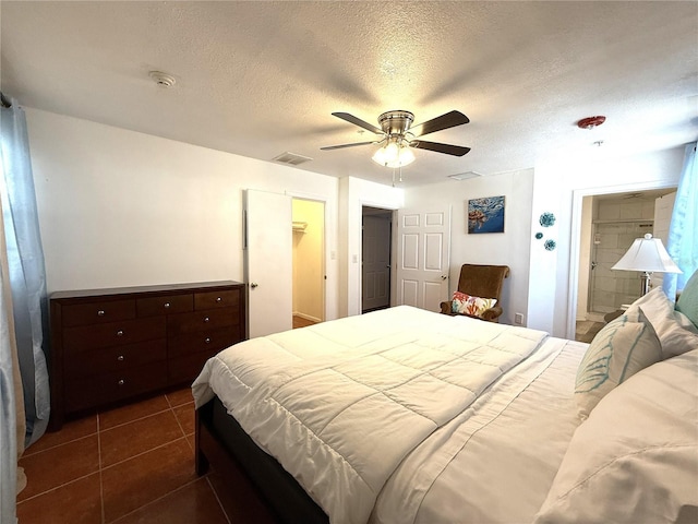 bedroom featuring ensuite bathroom, dark tile patterned flooring, a walk in closet, ceiling fan, and a textured ceiling