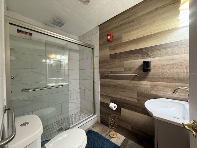 bathroom with wooden walls, vanity, a textured ceiling, toilet, and walk in shower