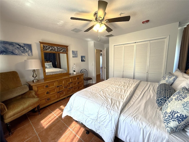 bedroom with tile patterned flooring, ceiling fan, a closet, and a textured ceiling