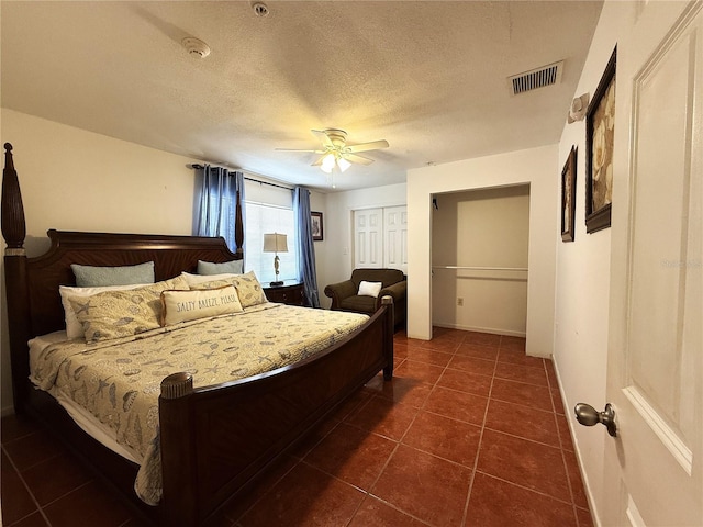 bedroom featuring dark tile patterned flooring, a closet, a textured ceiling, and ceiling fan