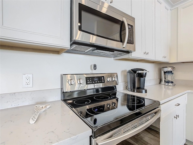 kitchen featuring white cabinetry, stainless steel appliances, light stone countertops, and wood-type flooring