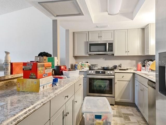 kitchen with light stone counters, stainless steel appliances, and gray cabinetry